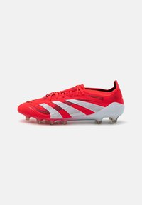 Red and white soccer cleat with a textured upper, featuring prominent three stripes design, plastic sole plate, and molded studs.