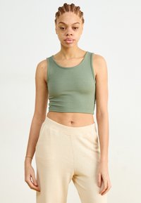 Green ribbed crop top with a round neckline, paired with cream-colored, soft-textured, wide-leg pants with side pockets.