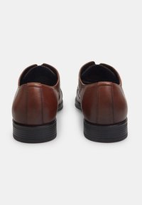 Scarpe di pelle marrone con una superficie liscia, forma arrotondata e suola in gomma nera. Presentano cuciture minime e un design elegante.