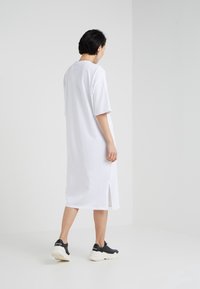 Biała, duża sukienka w T-shirt z krótkim rękawem, z bocznymi rozcięciami, luźny krój, wykonana z bawełny, zestawiona z czarnymi sneakersami sportowymi.