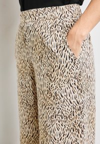 Pantalons à jambes larges en tissu doux et léger. Présente un motif animalier abstrait en noir et beige. Inclut des poches latérales et une taille élastique.