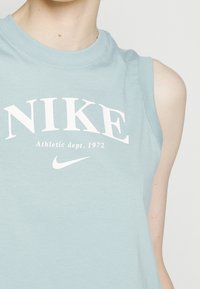Světle modrá bezrukávová sportovní košile vyrobená z měkké bavlny, s velkým bíl ým textem "NIKE" a logem, pod kterým je nápis "Athletic dept. 1972".