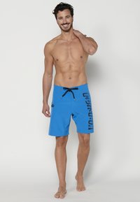 Bañador azul con un diseño de logo negro en el lateral, con una cinturilla ajustable y una tela suave y ligera.
