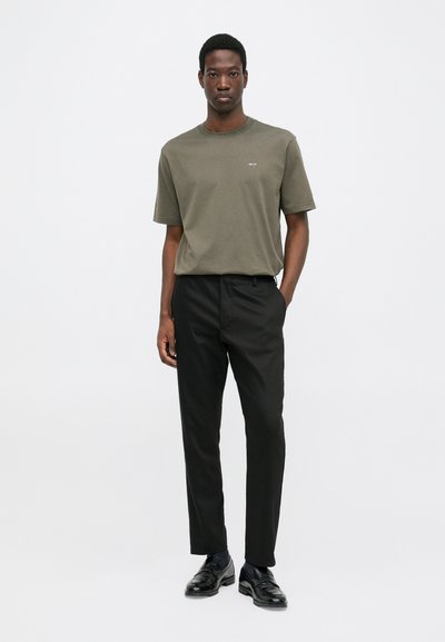 T-shirt in cotone verde oliva, maniche corte, colletto rotondo, abbinato a pantaloni neri slim-fit. Mocassini neri completano l'outfit.