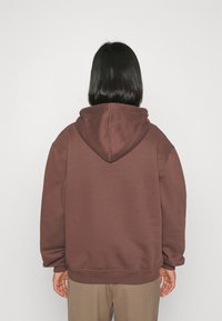 Braunes Kapuzen-Sweatshirt aus weichem Stoff, mit lockerem Schnitt, gerippten Bündchen und einer angenähten Kapuze. Schlichtes Design ohne zusätzliche Muster.