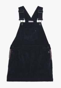 Tmavě modré lacláče z manšestru s nastavitelnými ramínky, předním kapsou a knoflíkovými detaily. Boční kapsy mají proužkované zdobení. Texturovaný povrch látky.