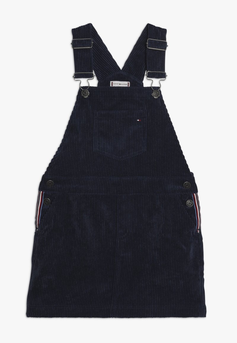 Tmavě modré lacláče z manšestru s nastavitelnými ramínky, předním kapsou a knoflíkovými detaily. Boční kapsy mají proužkované zdobení. Texturovaný povrch látky.