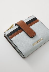 Portafoglio in pelle texturizzata con un corpo azzurro chiaro, dettagli marroni e strisce nere. Presenta un logo dorato e una chiusura a patta con una tasca con zipper.