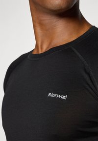 Schwarzes, tailliertes T-Shirt aus glattem Stoff. Mit rundem Halsausschnitt und kurzen Raglanärmeln. Mit weißem, gesticktem Logo auf der Brust.