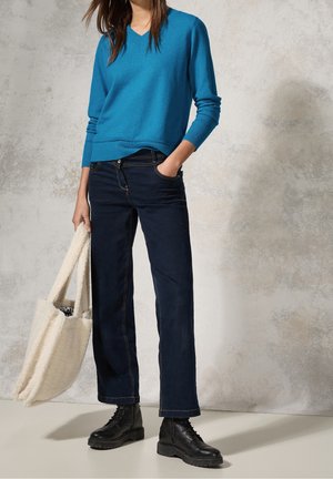Blauw v-hals gebreide trui, donkerblauwe wijde jeans en zwarte veterschoenen tot de enkel. Crème handtas met een textuur van bontpatroon.
