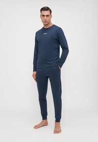 Set de îmbrăcăminte loungewear de culoare bleumarin, format dintr-un top cu mânecă lungă cu logo și pantaloni cu manșete elastice; textură netedă, croială lejeră.