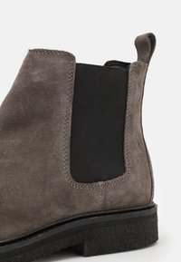 Botín de ante gris con paneles laterales elásticos. Suela plana negra con borde texturizado. Costuras de contraste a lo largo de las uniones.