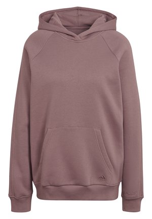 Person iført lilla Adidas-hoodie og matchende joggingbukser, med den ene hånd i frontlommen og synligt Adidas-logo på begge tøjdele.