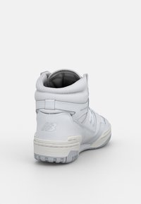 Białe trampki wysokie, wykonane z gładkiej skóry, z wyściełanym kołnierzem, gumową podeszwą i wytłoczonym logo na pięcie. Prosty design bez wzorów.