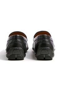 Zwarte lederen loafers met afgeronde achterkant, zichtbare stiksels en gestructureerde rubberen zolen. Minimalistisch ontwerp zonder extra versieringen.