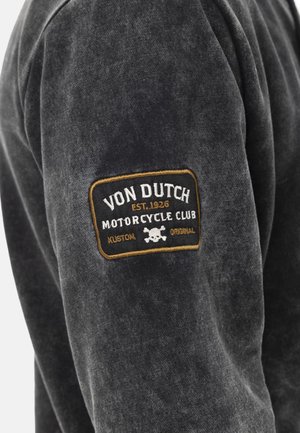 Sweatshirt noir en tissu doux avec un patch texturé. Le patch comprend "Von Dutch Motorcycle Club", un graphique de crâne et des accents dorés.