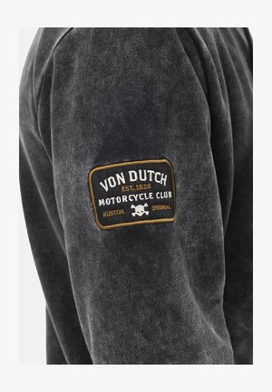 Sweatshirt noir en tissu doux avec un patch texturé. Le patch comprend "Von Dutch Motorcycle Club", un graphique de crâne et des accents dorés.
