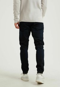 Tummansiniset jogging-tyyppiset housut, joissa on joustavat hihnat, kaksi takataskua ja sileä pinta, yhdistettynä vaaleisiin lenkkareihin.