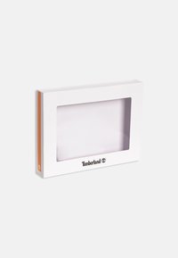 Packaging rectangular blanco con una ventana frontal transparente. Presenta acentos naranjas en un lado y el logo de Timberland impreso en el frente.