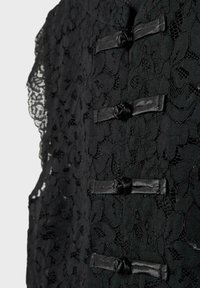 Gros plan sur un tissu en dentelle florale noire avec quatre fermetures nœud grenouille noires sur un vêtement texturé.
