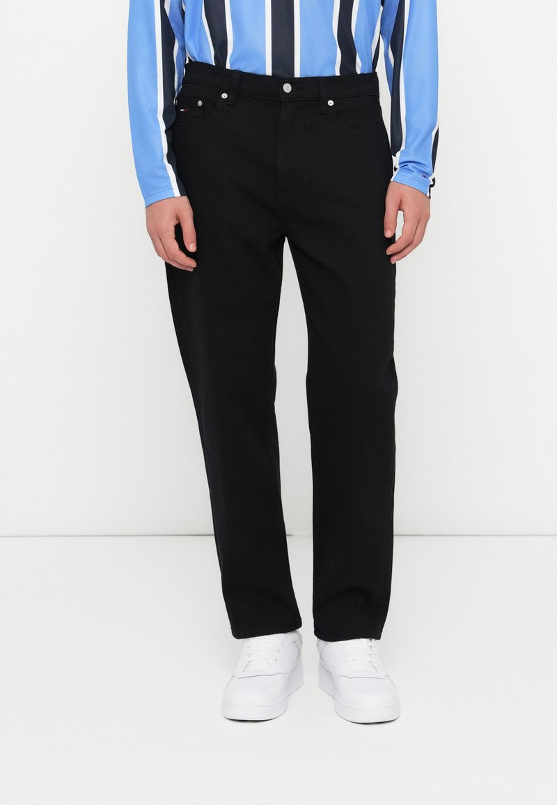 Czarne dżinsy o prostym kroju z klasycznym pięciopocketowym wzorem, z metalowymi elementami i zapięciem na guzik, w połączeniu z białymi sneakersami.