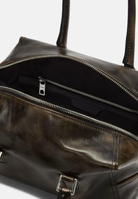 Dunkelbraune Ledertasche mit teilweise geöffnetem silbernen Reißverschluss, der einen schwarzen Innenraum und eine innere Reißverschlusstasche mit einem metallischen Markenanhänger zeigt.