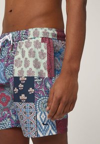 Plážové šortky v patchworkovom dizajne s kvetinovými a geometrickými vzormi v modrej, burgundskej a mentolovej zelenej farbe. Elastický pás so sťahovacou šnúrkou.
