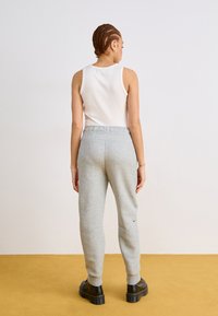 Pantalon de jogging gris avec taille élastique, poignets côtelés et un petit logo noir. Associé à un haut sans manches blanc et des bottes à plateformes noires.