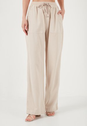 Beige weit geschnittene Hose aus leichtem Stoff mit elastischem Bund und Kordelzug. Verfügt über zwei große Vordertaschen.