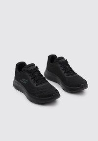 Czarne buty sportowe z przewiewną siateczką, wyściełanym kołnierzem i teksturowaną sole; posiadają sznurowaną konstrukcję oraz logo z boku.