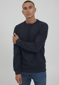 Navy crew-neck collegepaita paksusta puuvillakankaasta, jossa on ribbadut hihat ja helma sekä pieni logotunnus rinnassa.