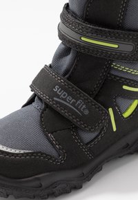 Chaussure d'extérieur pour enfants noire et grise avec semelle texturée, deux bandes Velcro ajustables et détails accentués vert citron vert.