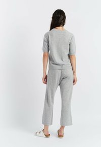 Maglione grigio a maglia con maniche corte, caratterizzato da un collo rotondo. Abbinato a pantaloni grigi a gamba larga e sandali bianchi. Tessuto liscio.
