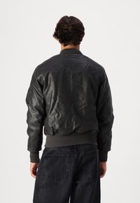 Black leather bomber jacket featuring a ribbed collar and cuffs, with a left sleeve pocket and a smooth, textured finish.