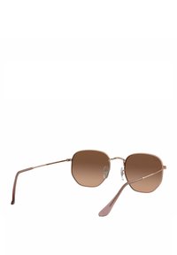 Gafas de sol con degradado marrón y un marco octagonal geométrico, brazos metálicos delgados y almohadillas nasales ajustables. El color general es un sutil metálico rosa.