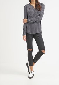 Långärmad blus i svart och vitt mönster med V-ringning, tillsammans med slitna svarta skinny jeans och vita slip-on skor.