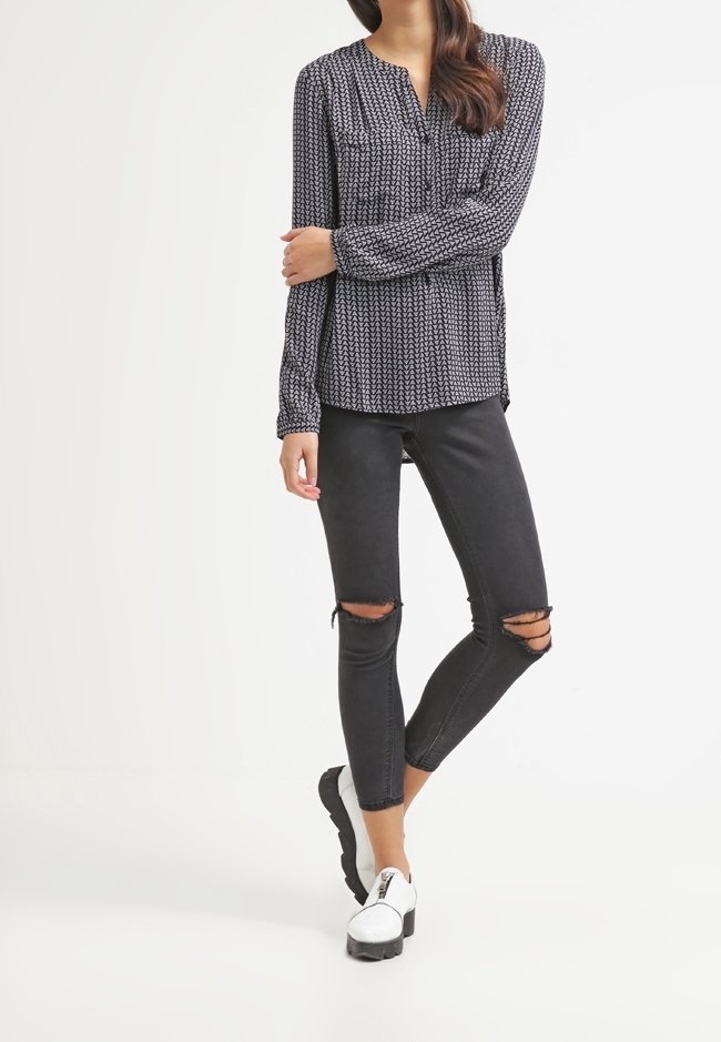 Långärmad blus i svart och vitt mönster med V-ringning, tillsammans med slitna svarta skinny jeans och vita slip-on skor.