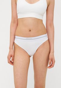 Caleçons blancs en coton avec une texture lisse, dotés d'une large ceinture élastique avec des rayures grises et un branding subtil.
