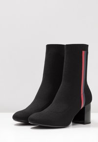 Botines de punto negros hasta el tobillo con punta cuadrada, que presentan un tacón ancho y sutiles rayas laterales rojas y azules. Tejido texturizado para un ajuste ceñido.