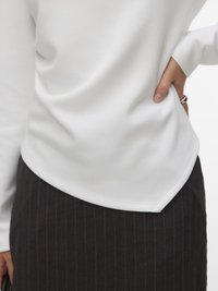 Person som har på seg en hvit langermet topp stukket inn i et mørkt, stripete skjørt, hånd på hoften med en sølvring synlig.