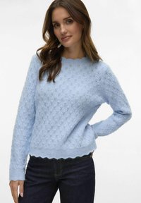 Lys blå strikket genser med et strukturert diamantmønster, scalloped halsutskjæring og nederkant, lange ermer, kombinert med mørk denim jeans.