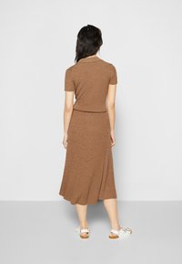 Vestido de malha canelada castanho com mangas curtas e cintura ajustada, fluindo para uma saia de comprimento médio. Usado com sandálias brancas.