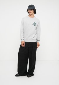 Sudadera gris con texto gráfico. Pantalones amplios negros con estampado y gorra negra. Tejido suave, corte relajado, diseño minimalista.