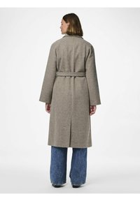 Lungo cappotto grigio in lana con cintura, spacco posteriore e maniche ampie, abbinato a jeans in denim blu a zampa di elefante. Design pulito e minimalista.