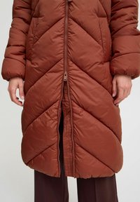 Brauner Wattierte Mantel mit einem Chevron-Steppmuster, Reißverschluss und gepolsterten Ärmeln. Glattes, leichtes Material, das für kaltes Wetter geeignet ist.