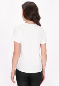 Hvid kortærmet t-shirt med rund hals, enkel design, blødt bomuldsstof og oprullede ærmer, båret med sorte tætsiddende bukser.