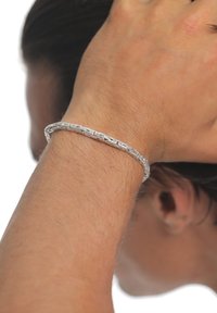 Silbernes Armband mit gewebtem Design, glatter Textur und schlankem Profil, getragen an einem Handgelenk mit hellem Hautton und sichtbarem Haar.