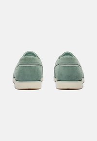 Mocassini in suede verde con un design a profilo basso, suola beige a contrasto e dettagli cuciti, visti da dietro.