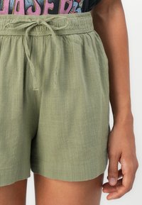 Olivgrüne Shorts mit elastischem Bund und Kordelzug. Leichter Stoff mit weicher Textur und lockerer Passform. Kurze Länge.