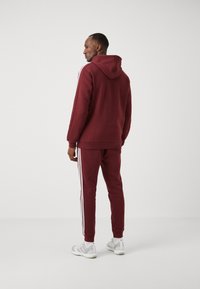 adidas Sportswear ESSENTIALS TAPERED CUFF 3-STRIPES  - Treniņtērpa apakšdaļas - shadow red